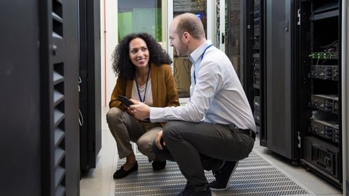 4 Reasons to Make the Switch to Outsourced IT Services Image description: A woman and a man crouching in front of data center technology making direct eye contact and smiling.